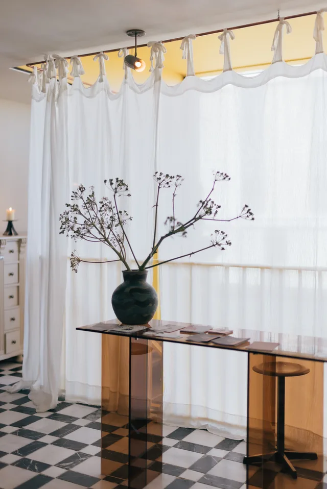 Vase with dried flowers in front of sheer curtains